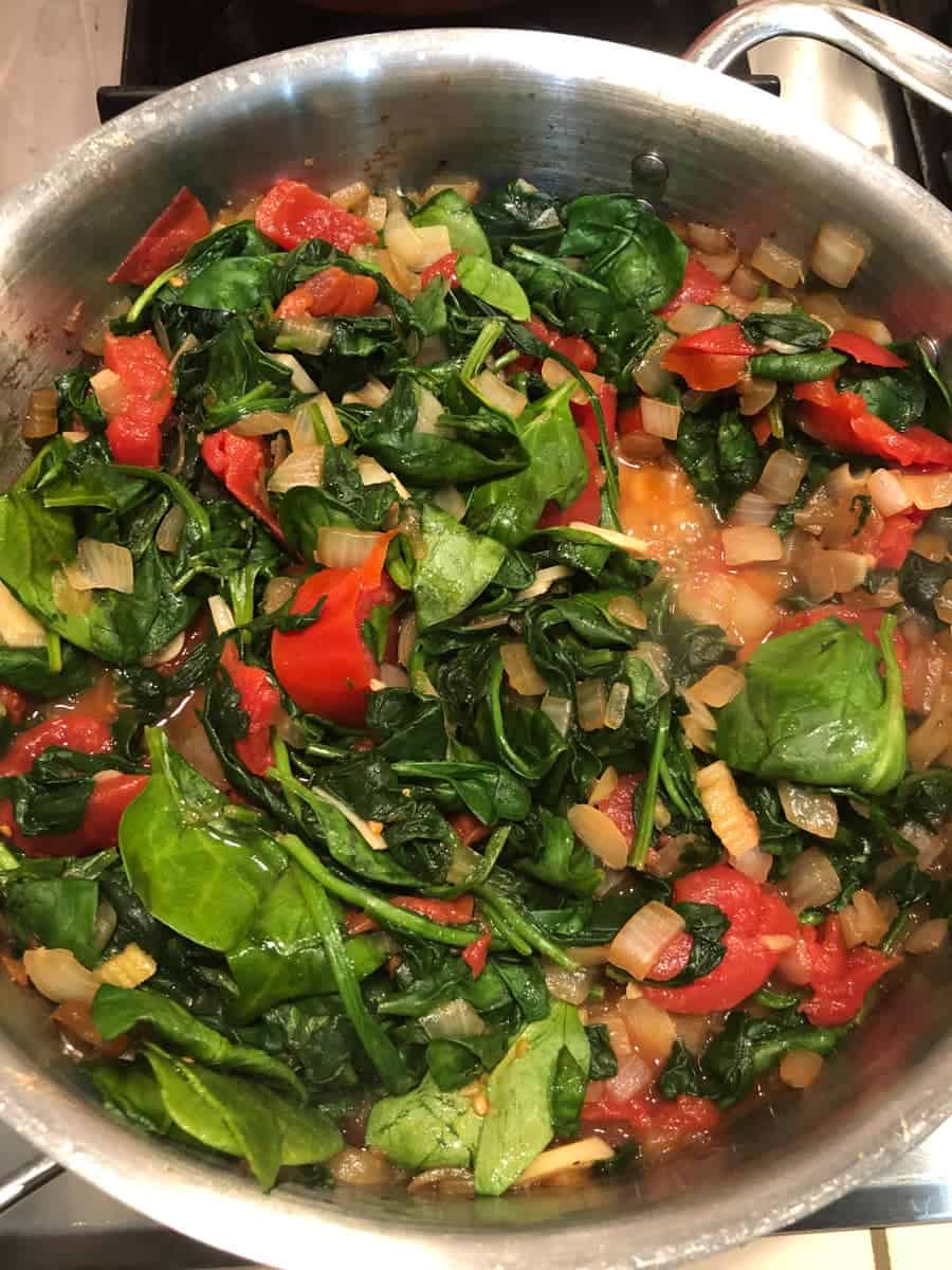 spinach, tomatoes, onion and garlic in pan cooking