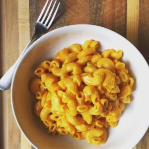vegan mac and cheese in white bowl with metal fork on wooden background