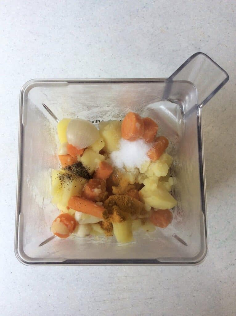 ingredients (cooked potato, carrot, onion, garlic and seasonings) in blender on counter