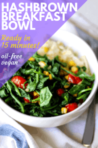 hash browns in a white bowl with sautéed spinach, corn, tomato