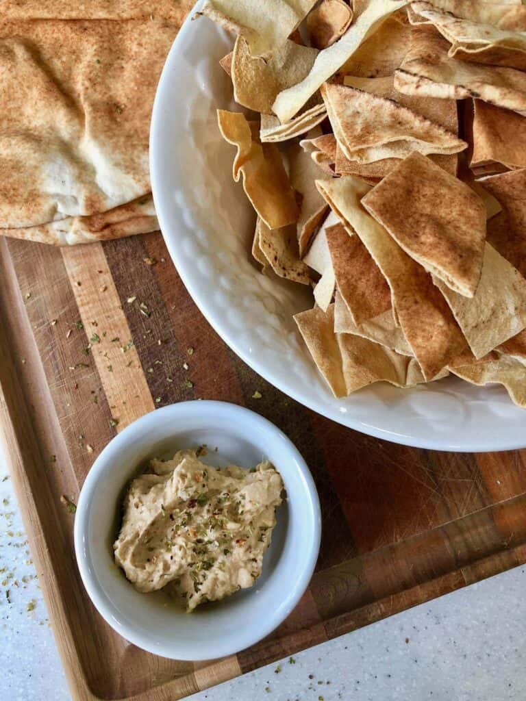 homemade pita chips in bowl with hummus and pita bread in background