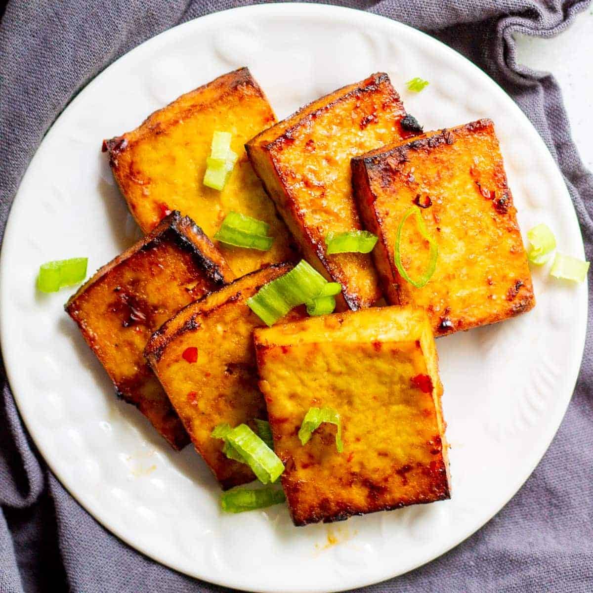 Sweet chili tofu rectangles on a white plate with green onions on top