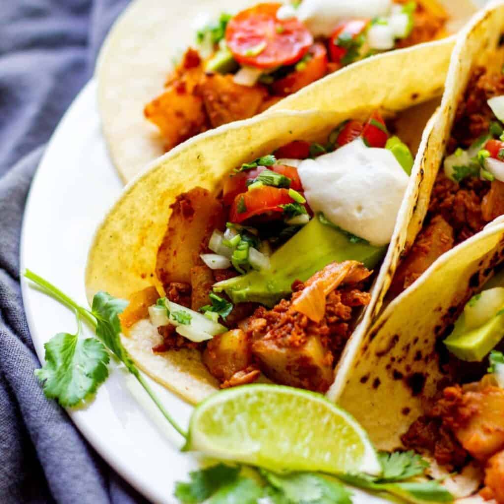 closeup of vegan soy chorizo and potato tacos with pico and sour cream on top