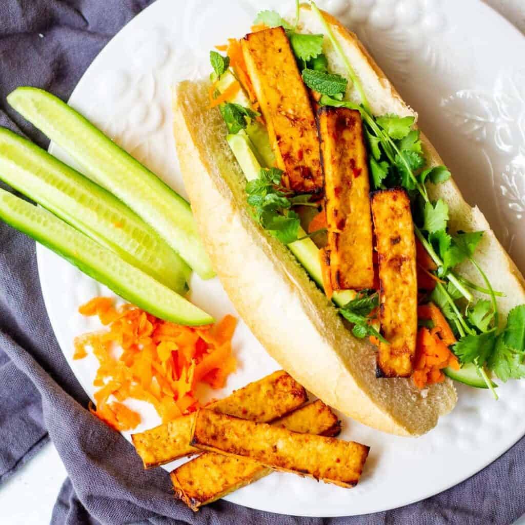 vegan banh mi sandwich with sweet chili air fryer tofu and sliced cucumbers on side