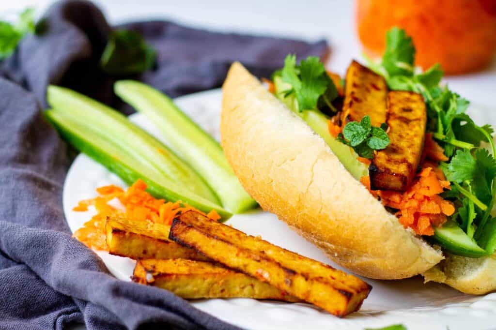 vegan banh mi sandwich with sweet chili air fryer tofu and sliced cucumbers on side