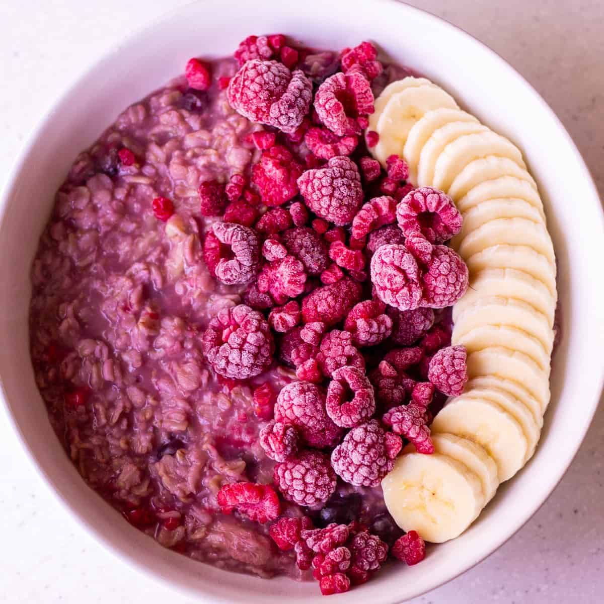 bowl of cherry berry oatmeal with frozen raspberries and sliced banana on top