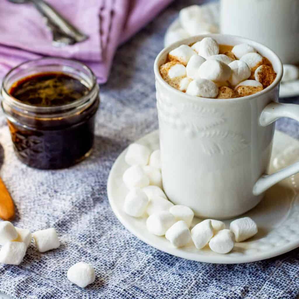 mug of pumpkin spice steamer with marshmallows and pumpkin spice simple syrup on side