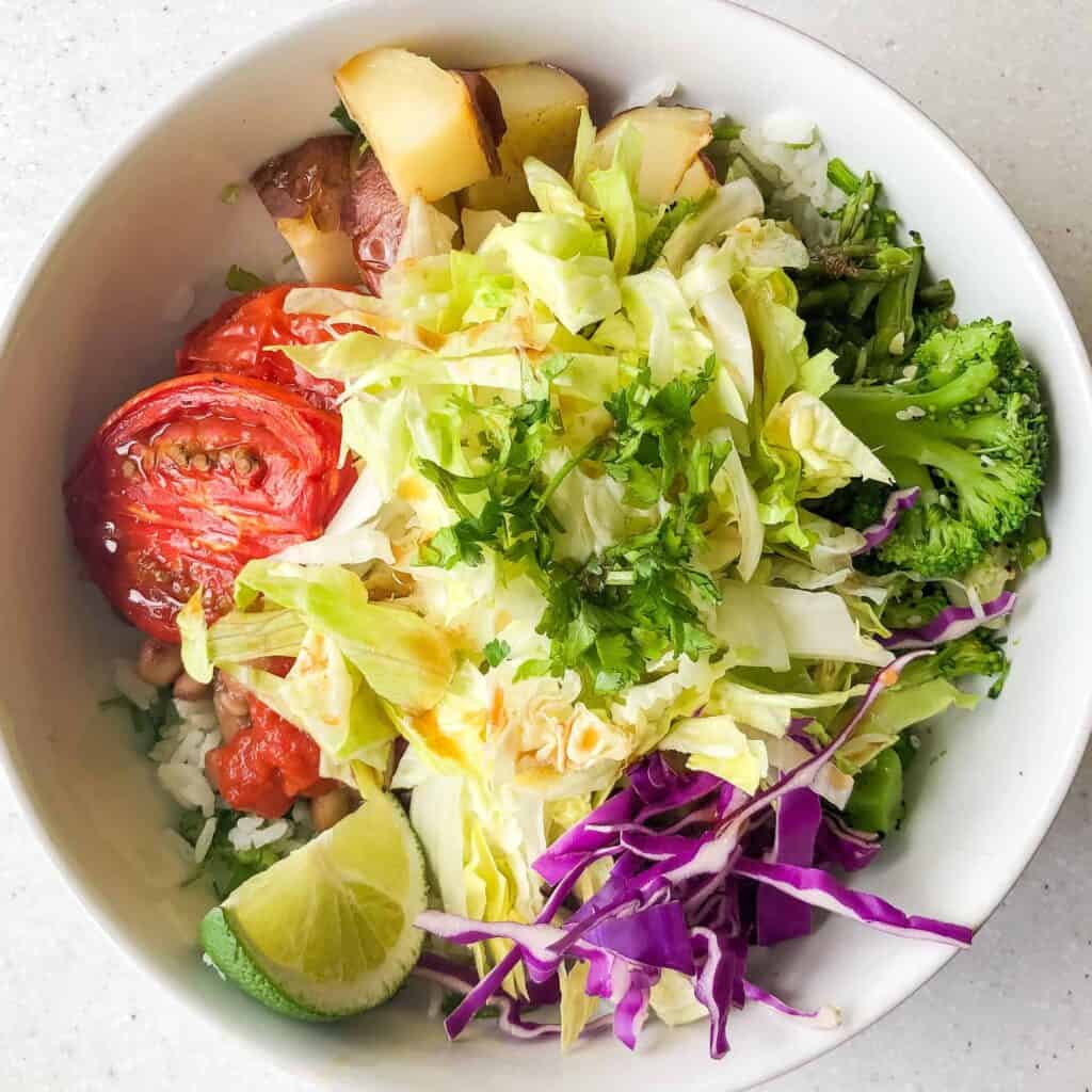 Burrito bowl with cilantro lime rice, potatoes, roasted tomatoes, broccoli, lettuce, cabbage, lime. Example of a 50/50 plate for plant-based weight loss.