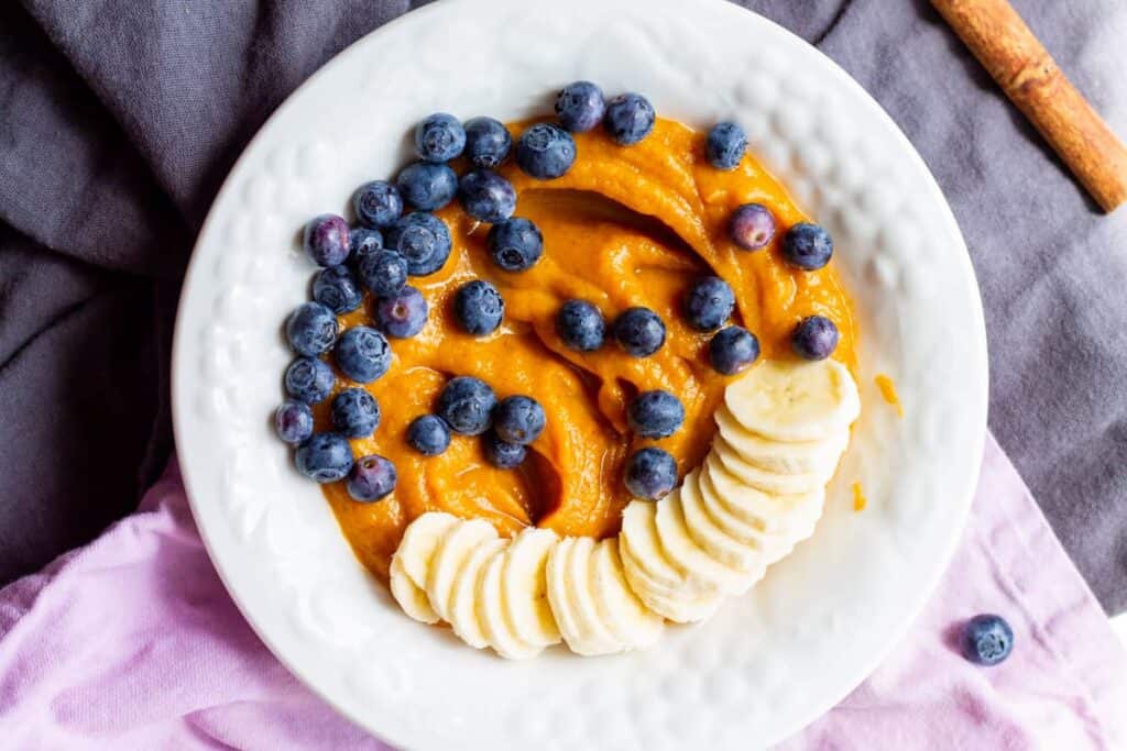sweet potato pudding in white bowl with blueberries and banana