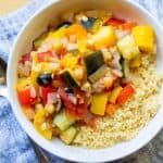 vegetable stew over couscous in white bowl with placement and spoon
