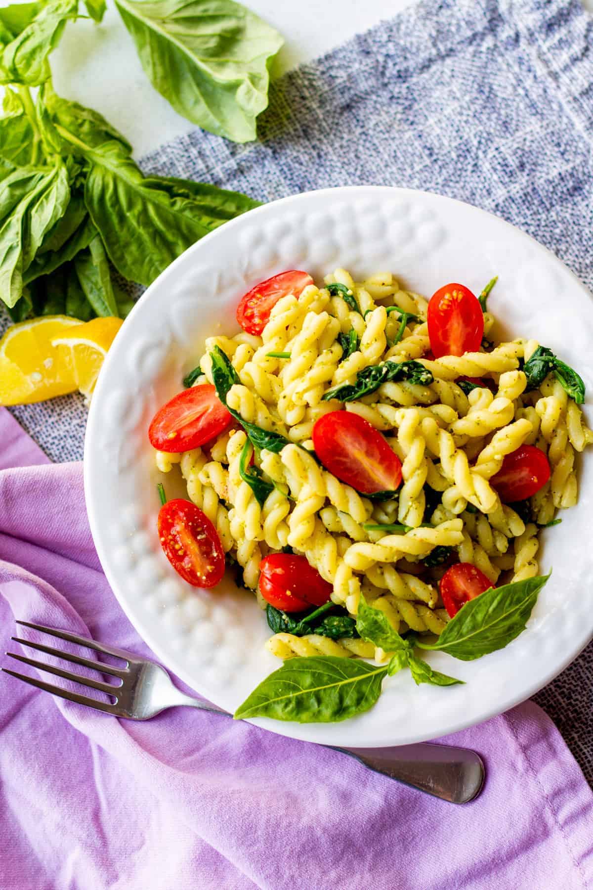 pasta in bowl with fork, napkin, lemon and basil leaves