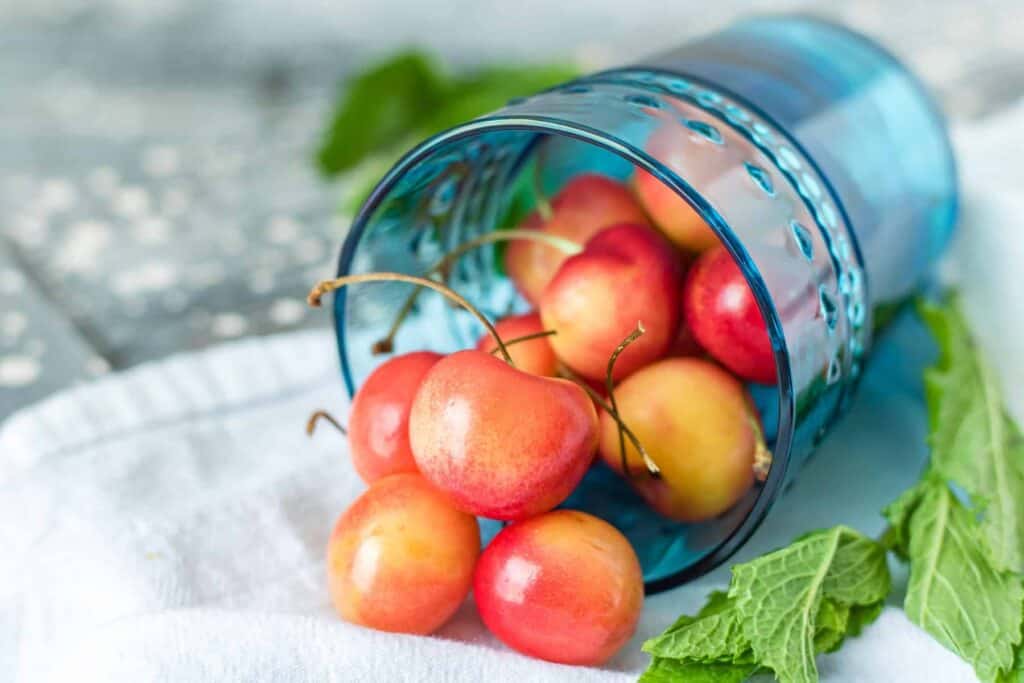 pink peach rainier cherries pouring out of blue glass