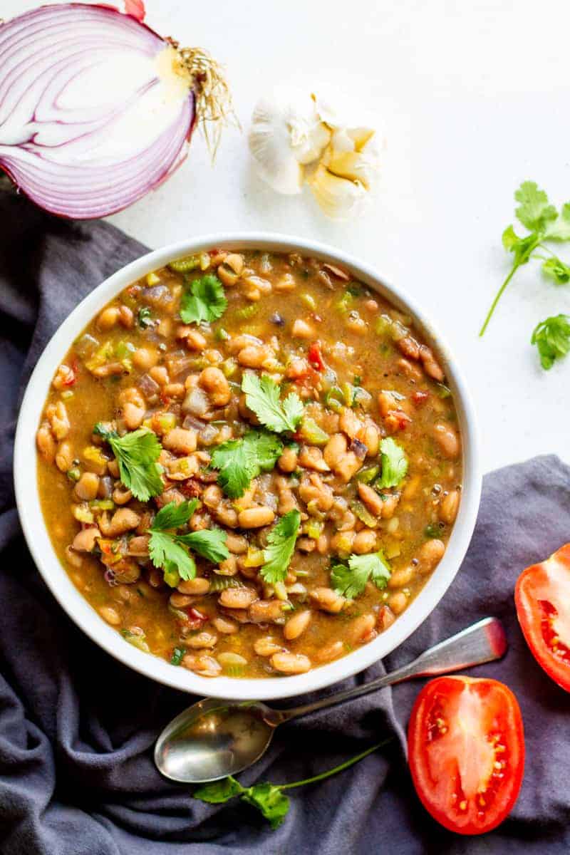 bowl of charro beans with spoon and onion and tomato on table