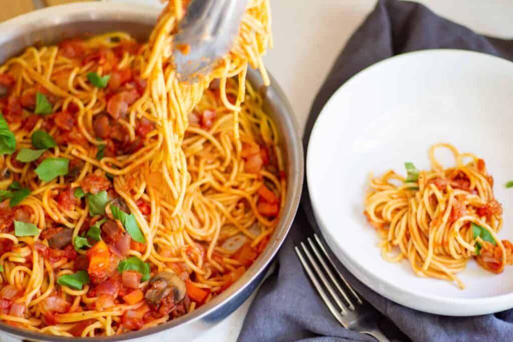 serving spaghetti with tongs into bowl