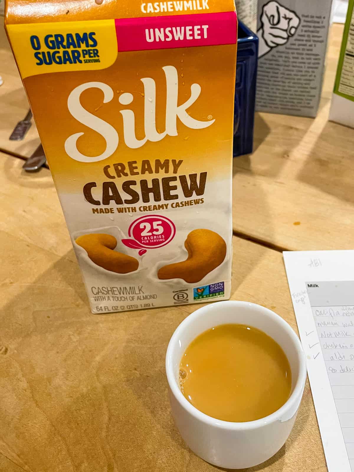 carton of silk creamy cashew milk with cup of hot black tea in front