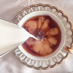 pouring soy milk into black tea in a teacup