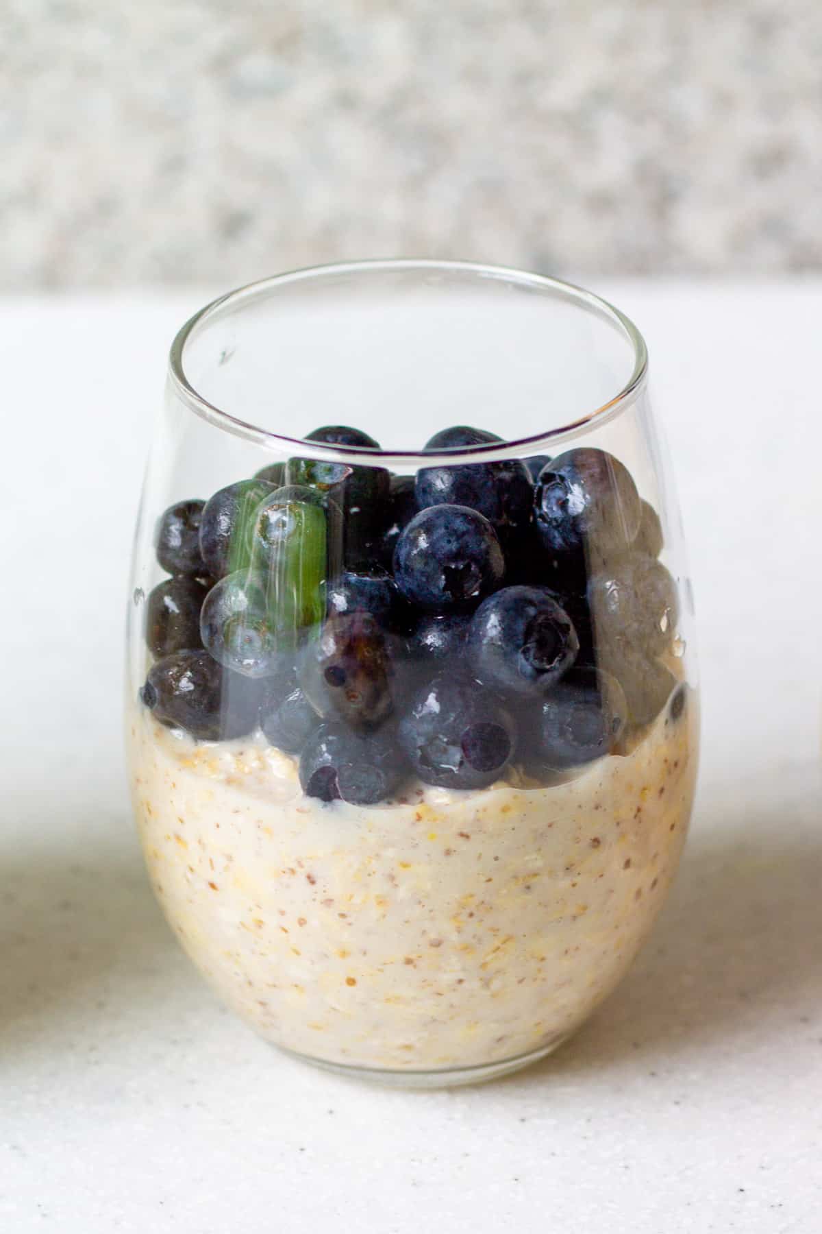 glass with vegan overnight oats and fresh blueberries on top