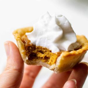 holding a mini pumpkin pie with a bite taken out