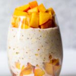 glass with vegan overnight oats and fresh peaches on top