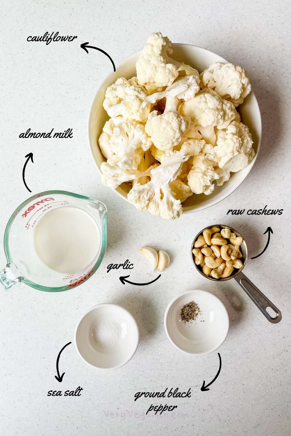 prepped ingredients laid out: cauliflower florets, almond milk, raw cashews, garlic, sea salt and ground black pepper