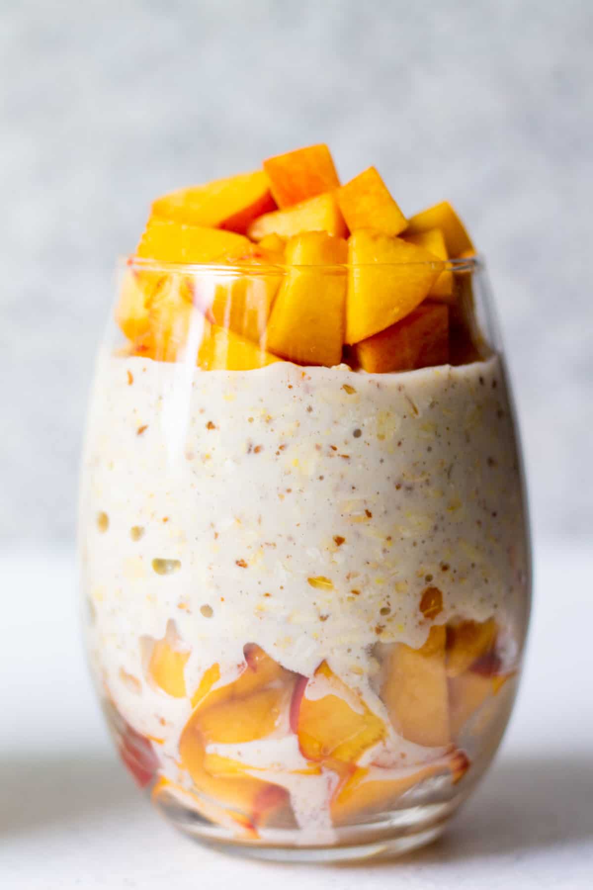 glass with vegan overnight oats and fresh peaches on top