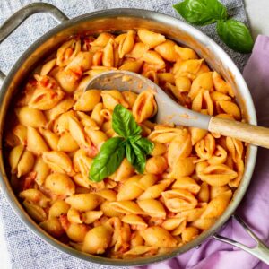 creamy tomato shell pasta in pan with fresh basil