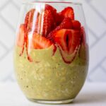 pretty glass with matcha overnight oats and sliced strawberries on top