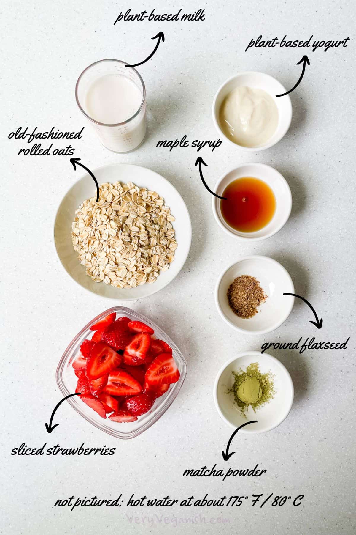 Ingredients laid out for matcha strawberry overnight oats: plant-based milk, plant-based yogurt, rolled oats, maple syrup, ground flax, sliced strawberries, hot water and matcha powder