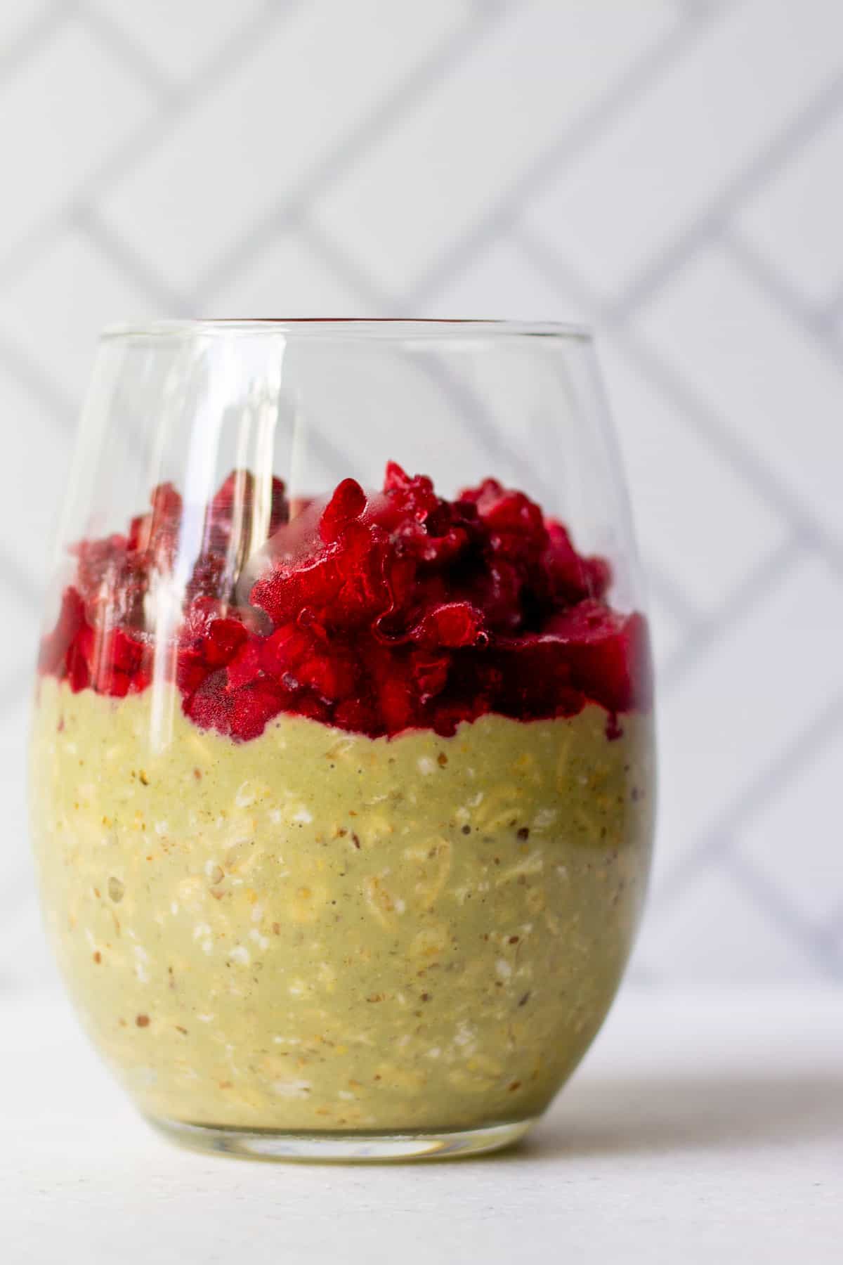 pretty glass with matcha overnight oats and thawed, frozen raspberries on top