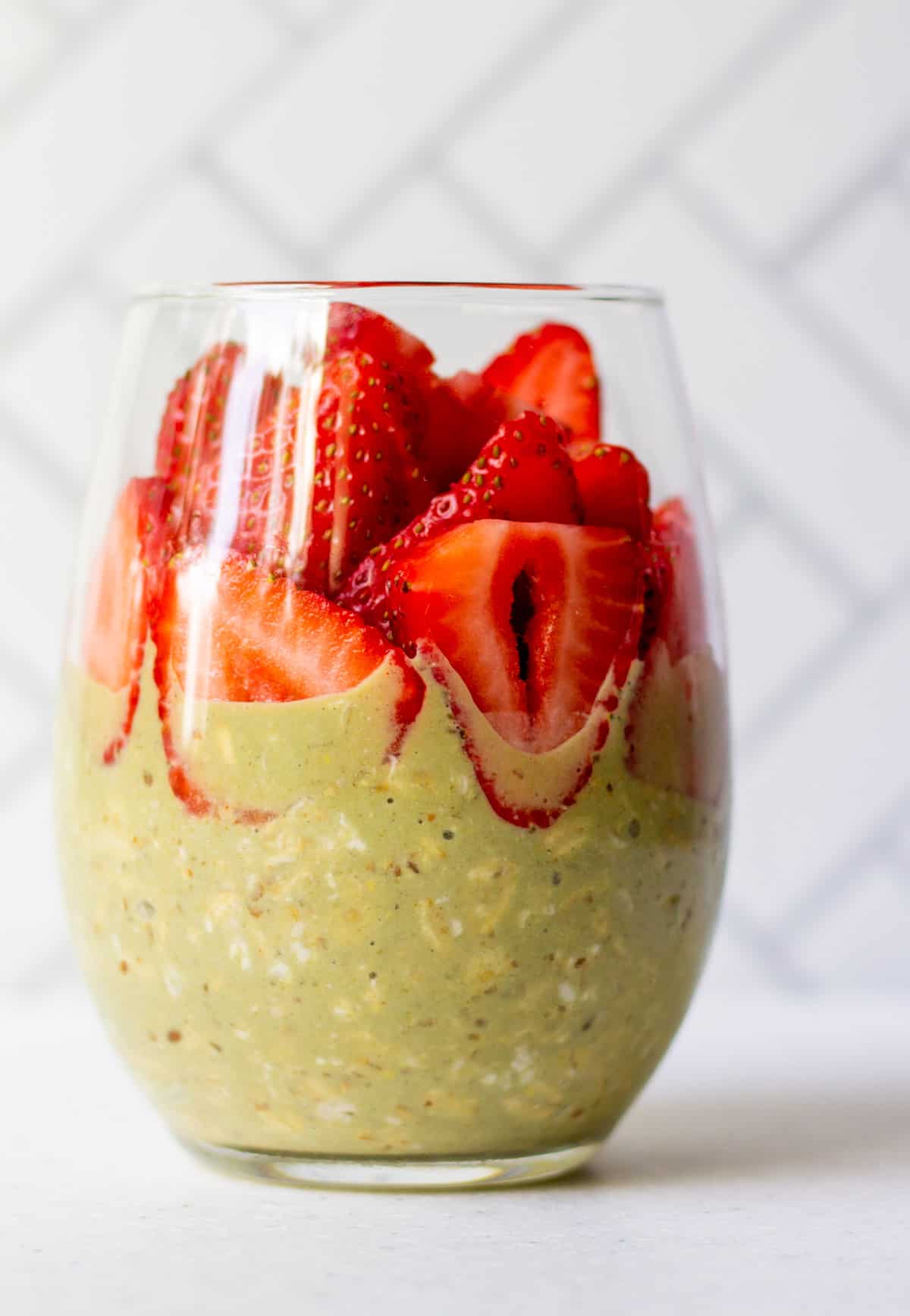 pretty glass with matcha overnight oats and sliced strawberries on top
