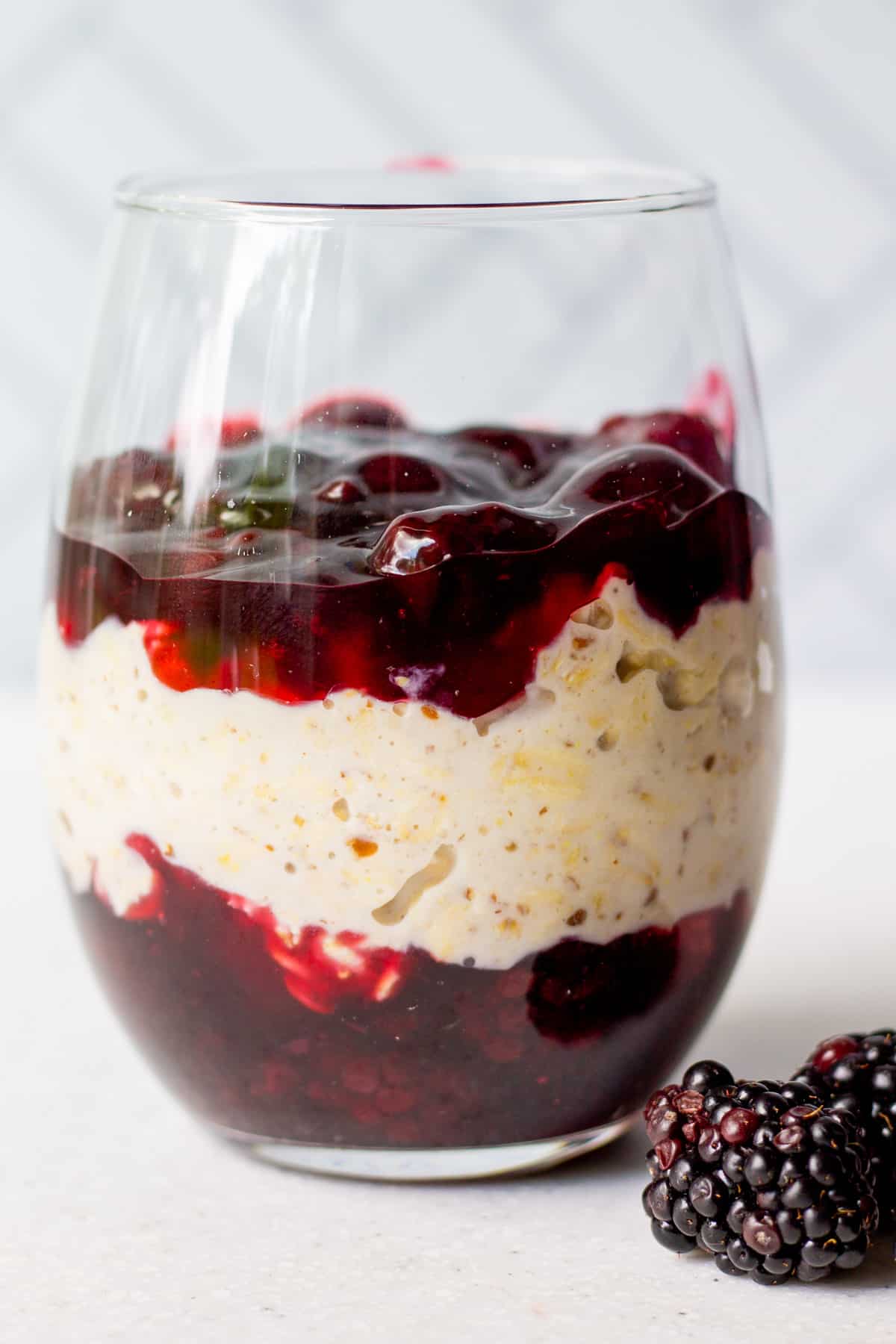 glass full of premium blackberry pie filling and overnight oats with fresh blackberries on side
