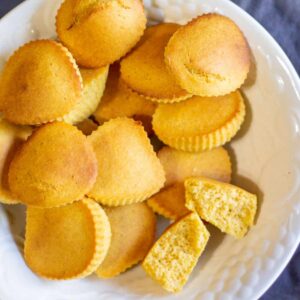 big white bowl of cornbread muffins with one cut open