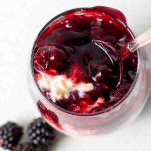glass full of premium blackberry pie filling and overnight oats with spoon and fresh blackberries on side