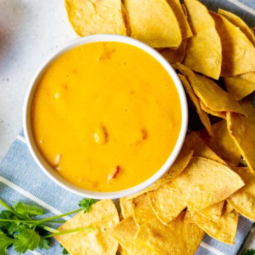 bowl of queso with chips around it and cilantro on the side
