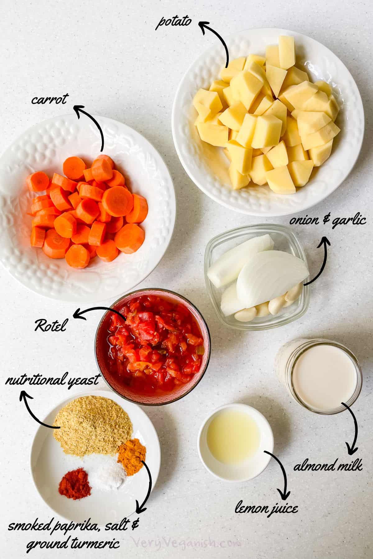 Ingredients laid out for vegan potato carrot nacho cheese rotel dip: cubed potato, sliced carrot, onion slices, garlic cloves, rotel, almond milk, lemon juice, nutritional yeast, smoked paprika, salt and ground turmeric