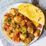 white plate full of papas a la mexicana (spicy Mexican-style breakfast potatoes) with two corn tortillas on the side