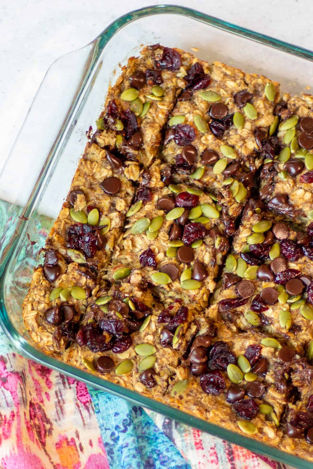 glass baking dish with baked banana oat bars topped with chocolate chips, dried cranberries and pepitas