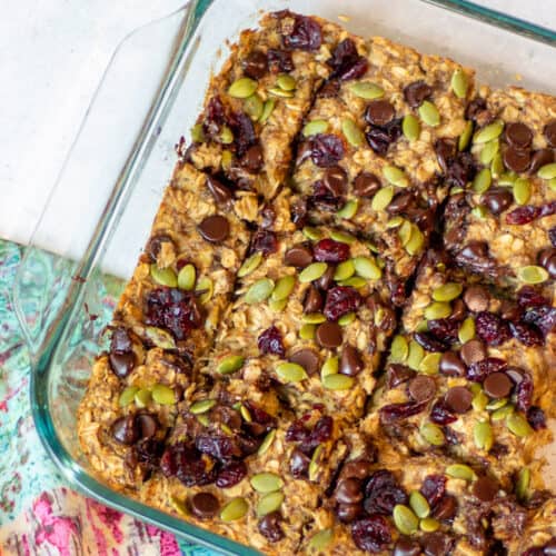 glass baking dish with baked banana oat bars topped with chocolate chips, dried cranberries and pepitas