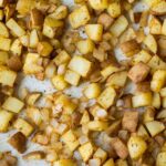 diced potato and onion after baking with spices on a parchment paper lined sheet pan