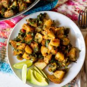 white plate of potatoes and kale, with lime and avocado