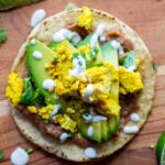 tostada with refried beans, sliced avocado, tofu scramble, crema and cilantro on a wooden board