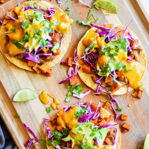 tostadas with beans, roasted sweet potato, red cabbage, avocado, vegan queso and cilantro on a wooden board