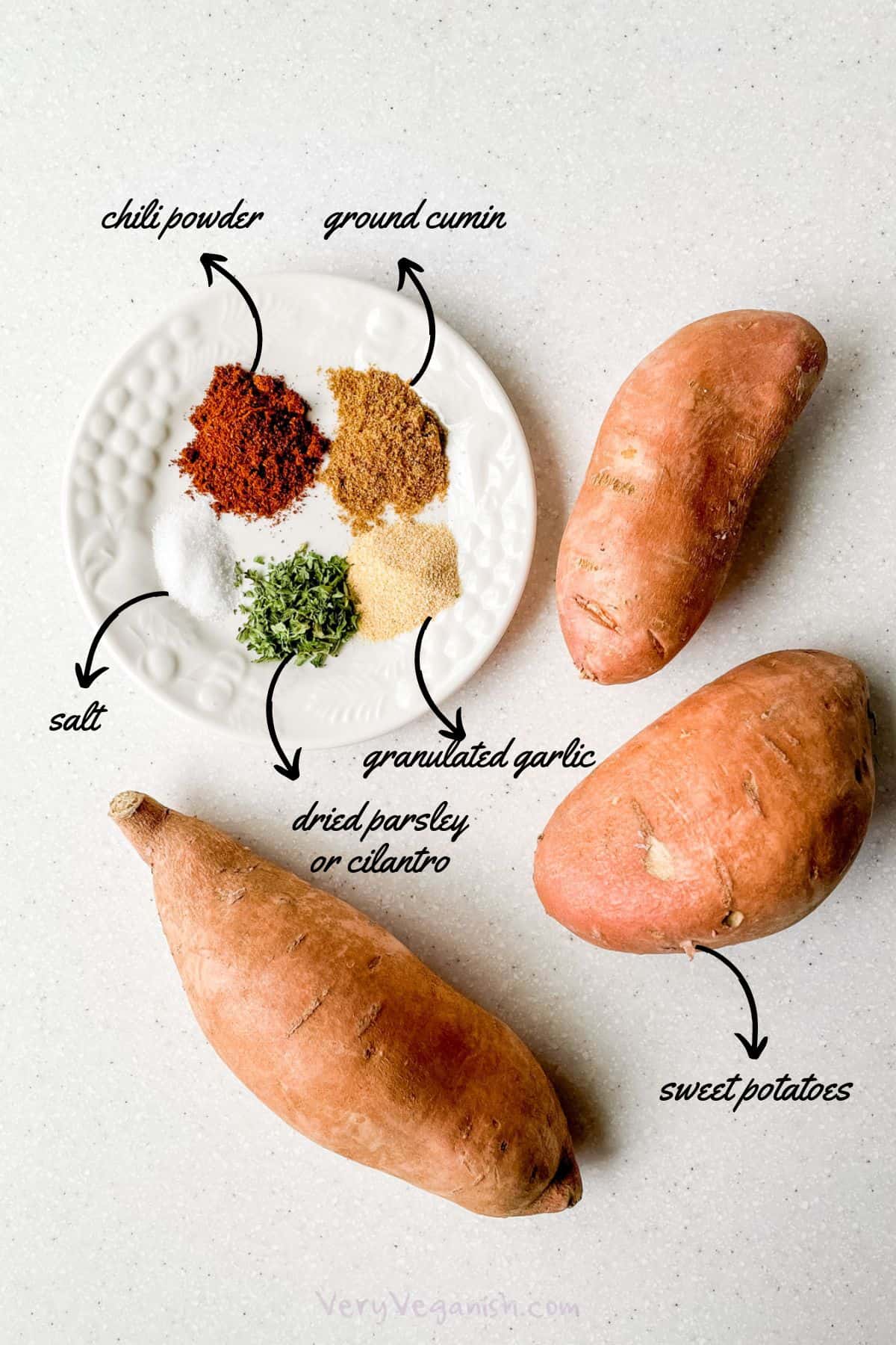 Ingredients laid out on counter: sweet potatoes, chili powder, ground cumin, granulated garlic, dried parsley and salt