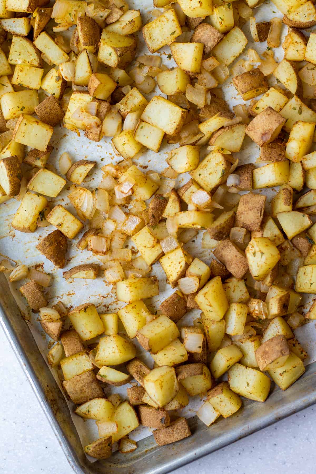diced potato and onion after baking with spices on a parchment paper lined sheet pan