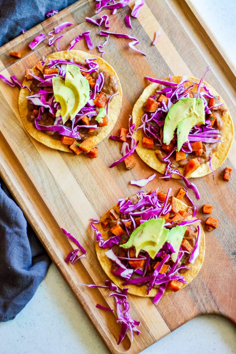 tostadas with beans, roasted sweet potato, red cabbage, avocado on a wooden board