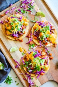tostadas with beans, roasted sweet potato, red cabbage, avocado, vegan queso and cilantro on a wooden board