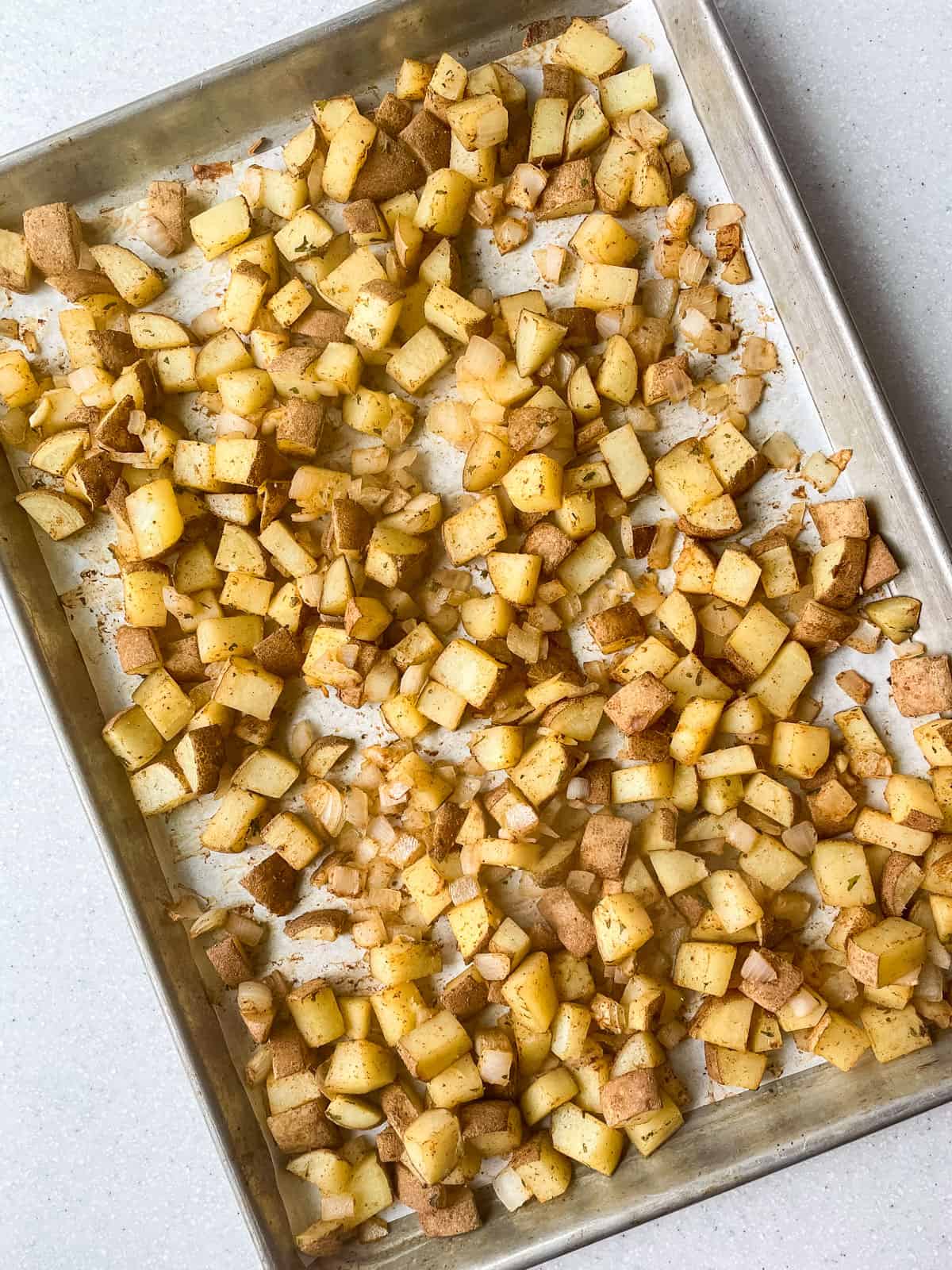 diced potato and onion after baking with spices on a parchment paper lined sheet pan
