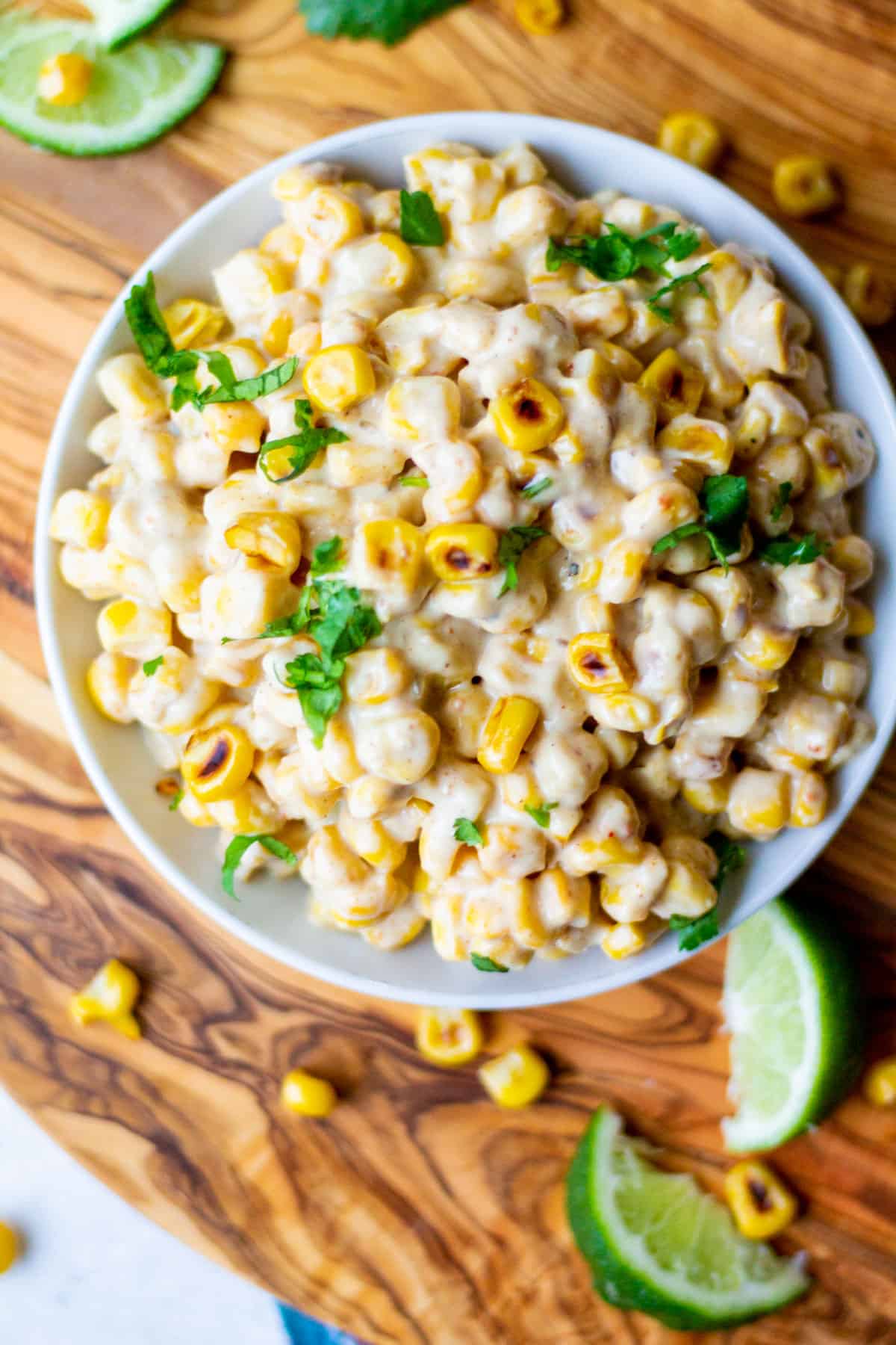 creamy spicy mexican-style street corn in a white bowl with cilantro sprinkled on top and limes on the side