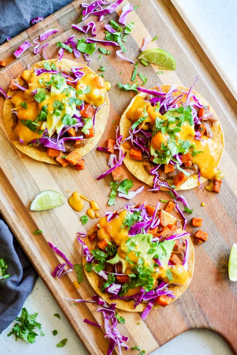 tostadas with beans, roasted sweet potato, red cabbage, avocado, vegan queso and cilantro on a wooden board