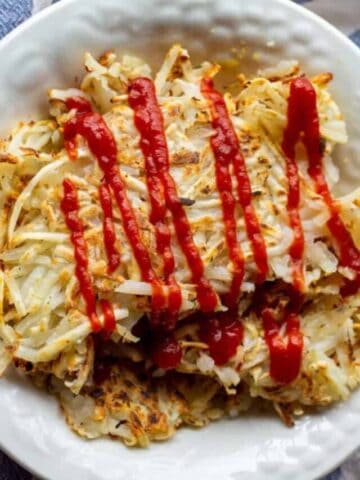Healthy Hash Browns with red drizzled ketchup on top in a bowl.